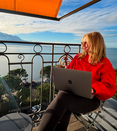 Cheryl working from a balcony table above a bright blue bay