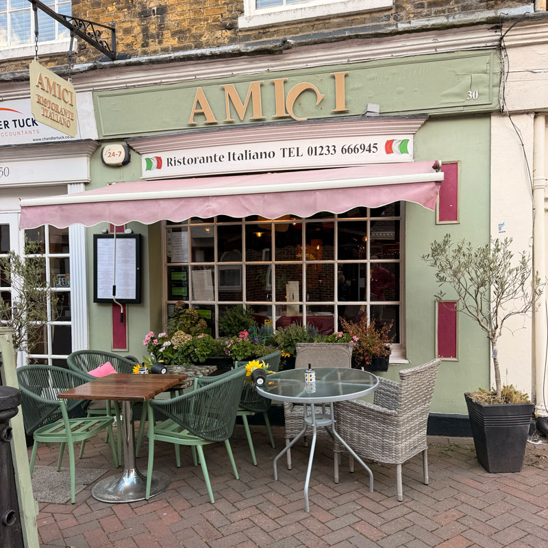 Sage green exterior of Amici Ristorante Italiano with gold lettering and pink awning, Ashford