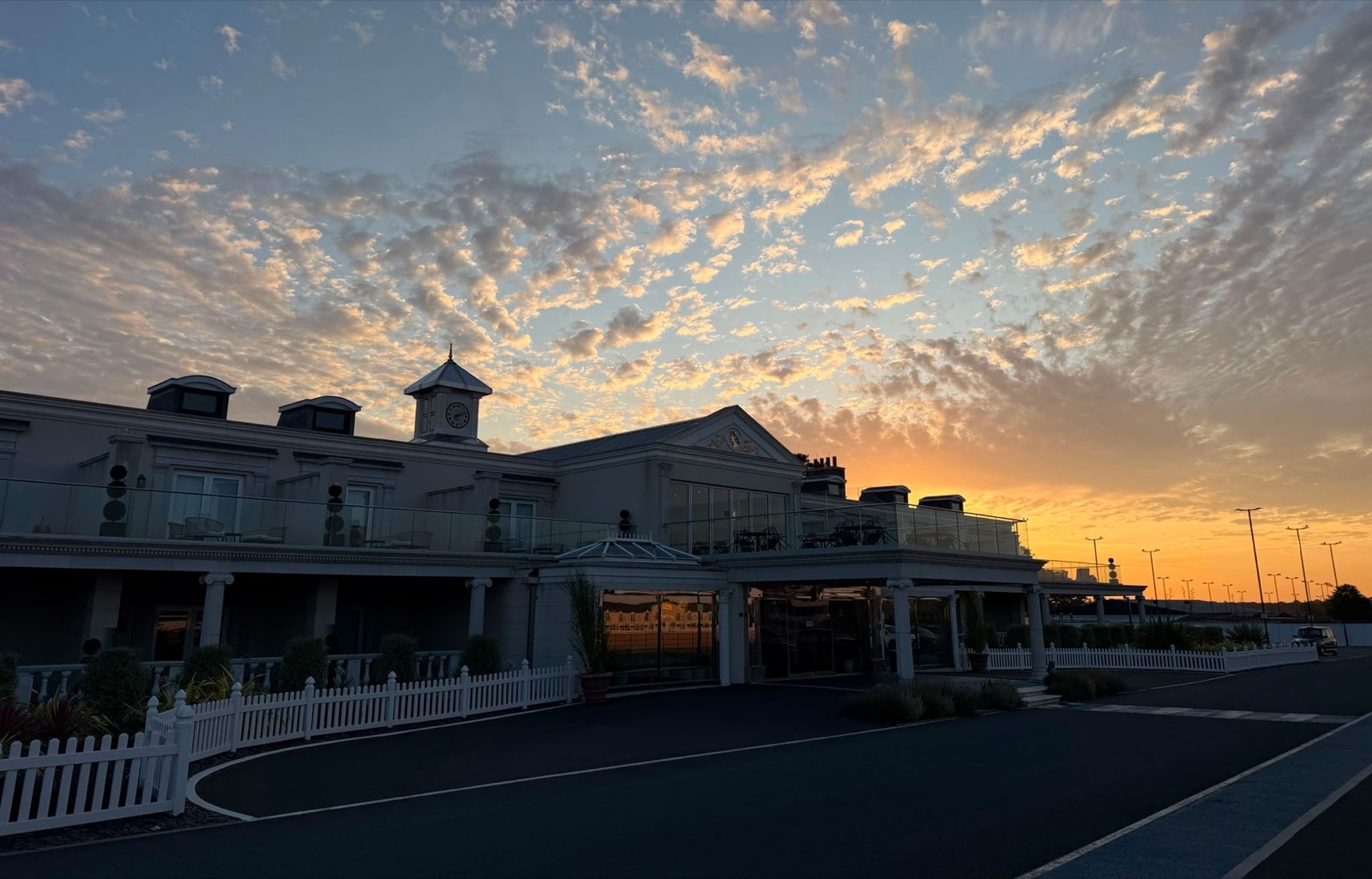 The Polo Club Hotel at sunset, its clock tower and colonnade silhouetted against an orange sky