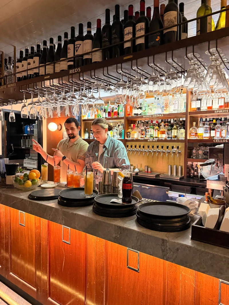 The bar at Blacklock Covent Garden, bartenders lining up long drinks under rows of hanging wine glasses