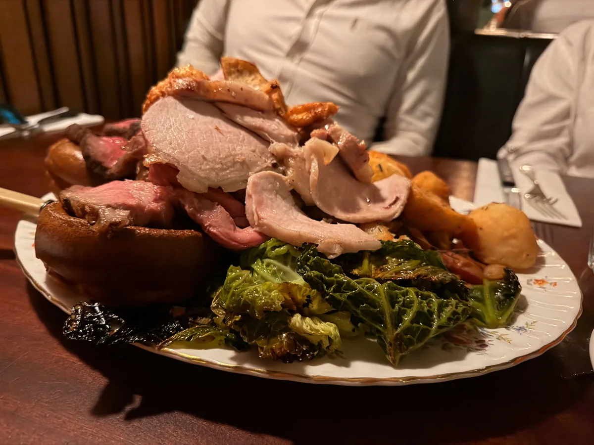 The Blacklock All In Sunday roast platter carried to the table, with beef rump, lamb leg, pork loin, a Yorkshire pudding and charred Savoy cabbage