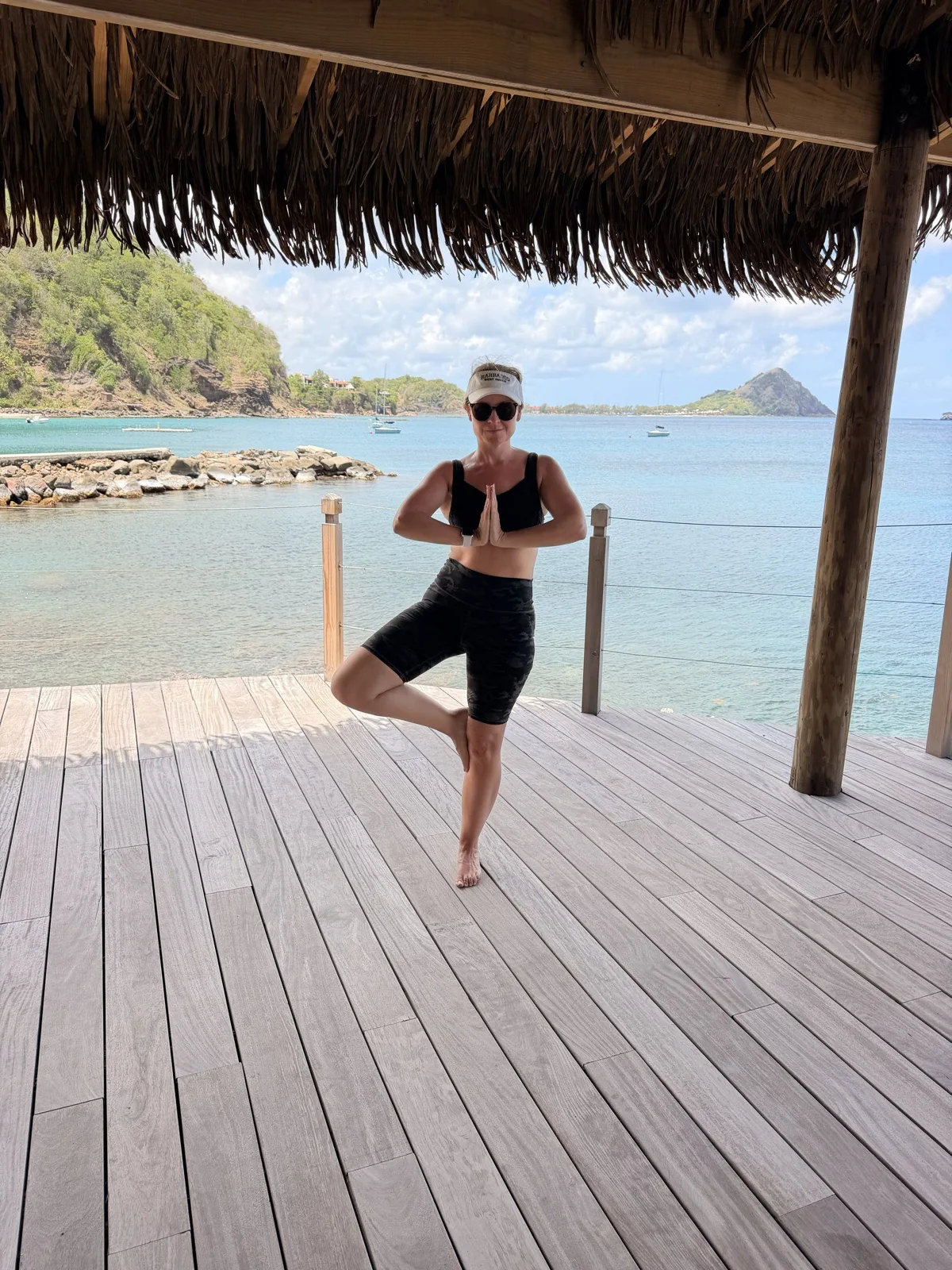 Tree pose on the open beach deck under a thatched roof, looking out over the bay
