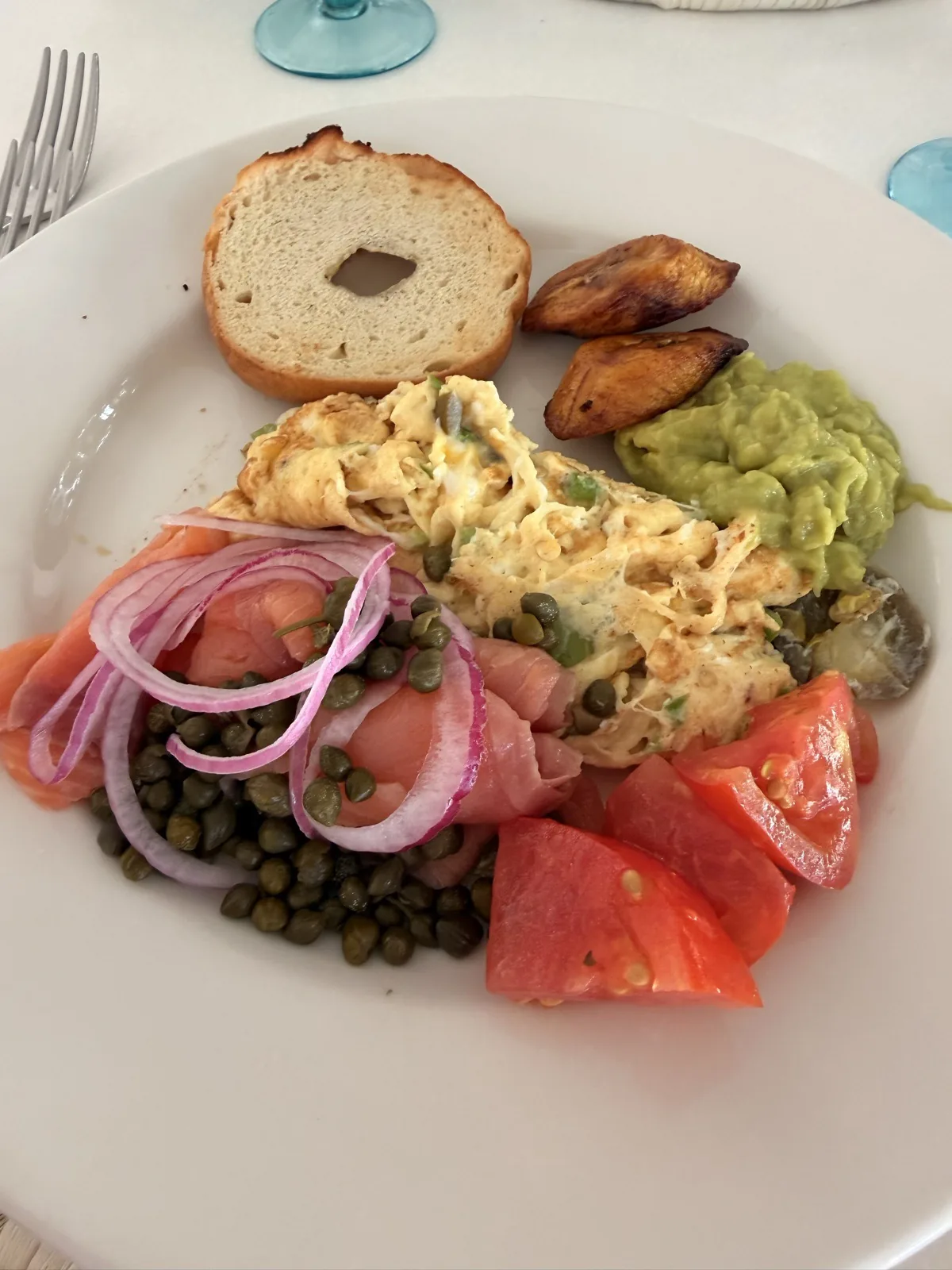 A breakfast plate of smoked salmon, capers, scrambled eggs, guacamole, tomato and plantain