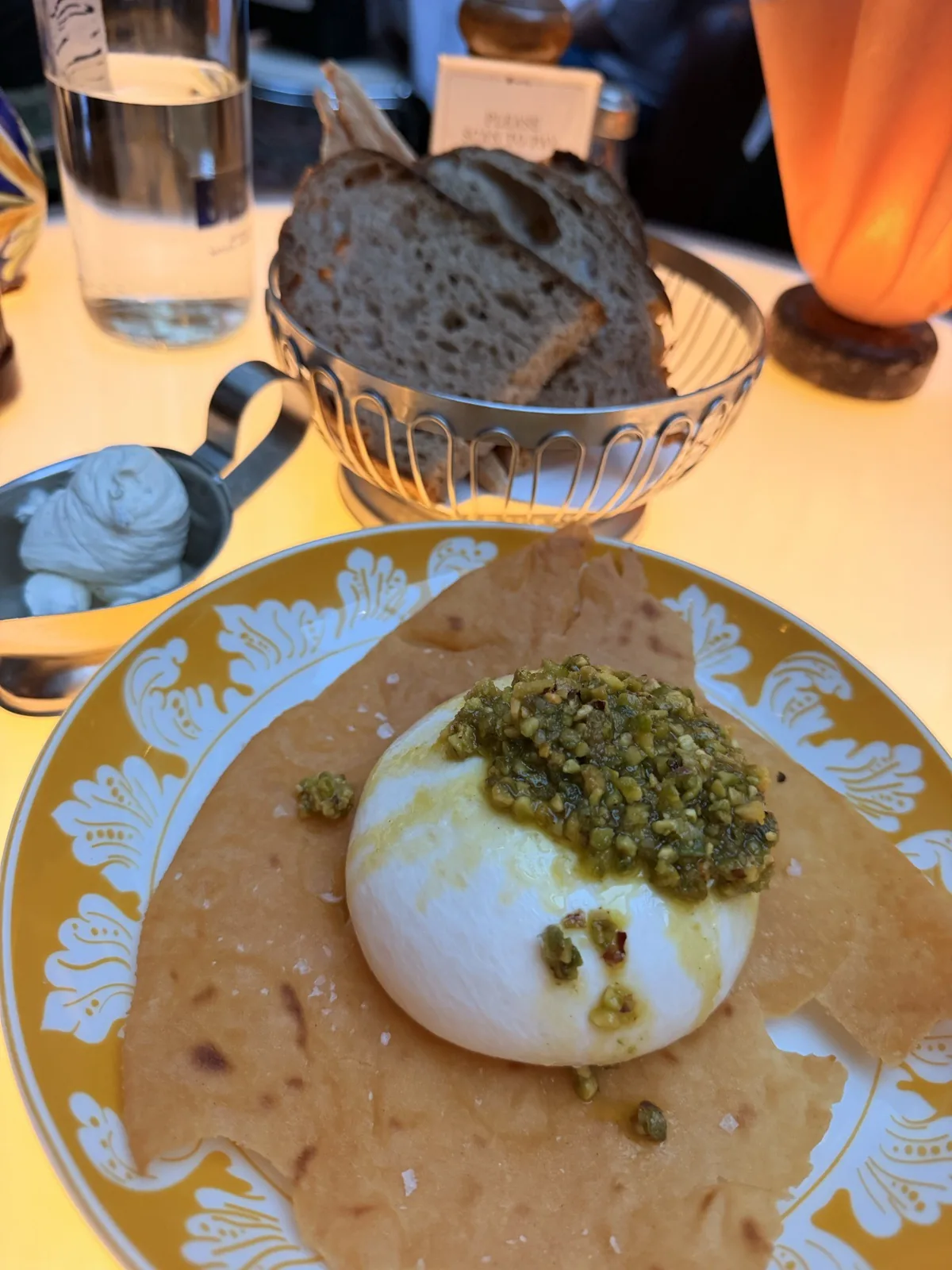 Burrata al Pistacchio with pistachio pesto on carasau bread, beside the bread basket at Carlotta