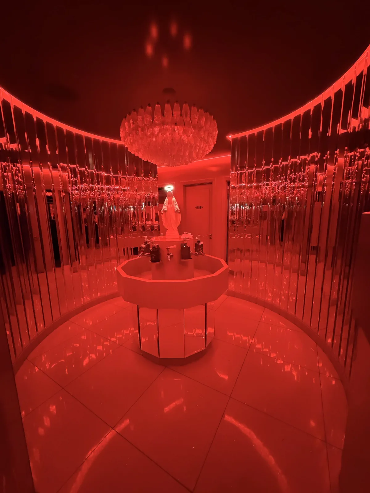 The mirrored circular bathroom at Carlotta Marylebone, washed in red light with a chandelier overhead