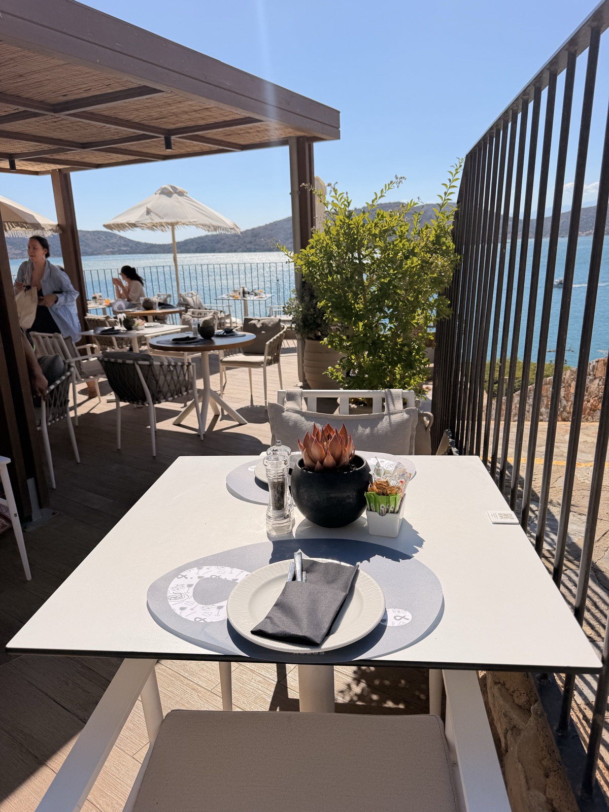 Breakfast table on the sea view terrace at Domes Aulus Elounda with parasols and Mirabello Bay behind