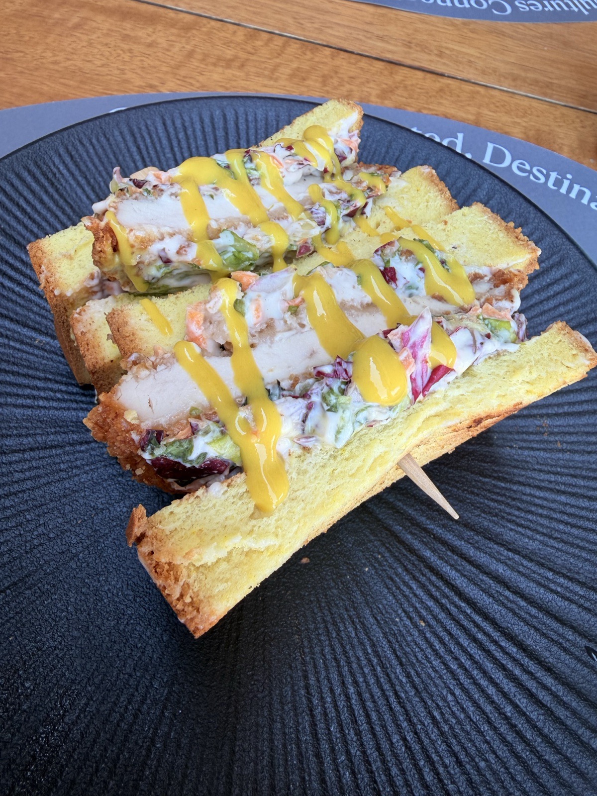 Crispy chicken club sandwich drizzled with mustard sauce served on a black plate