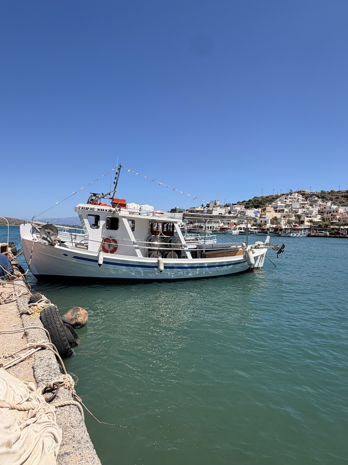 Traditional white and blue fishing boat in Elounda harbour with the village behind