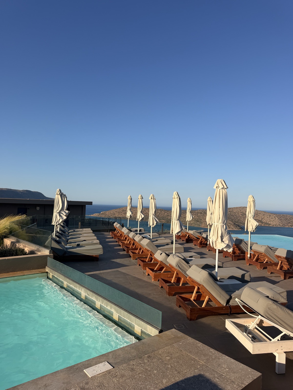 Rooftop pool and wooden sun loungers at Domes Aulus Elounda overlooking the sea at golden hour