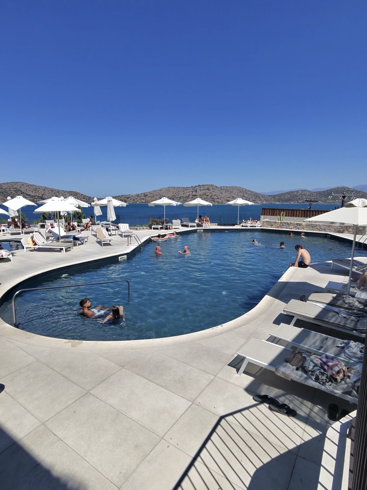 Curved main pool at Domes Aulus Elounda with white parasols and sea views towards the hills