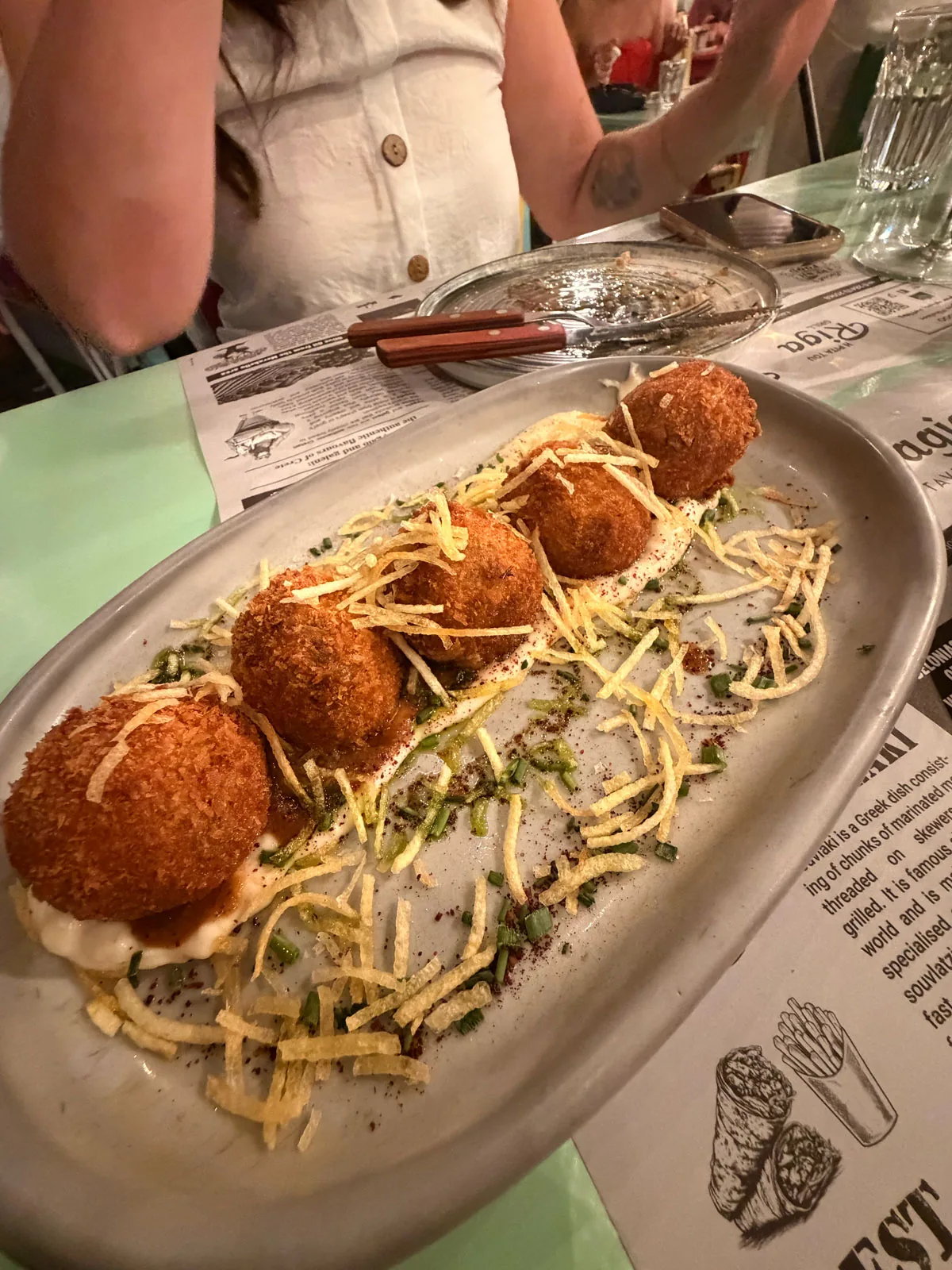 Five moussaka croquettes on a swoosh of cream with fine crispy potato threads on top at Karnagio