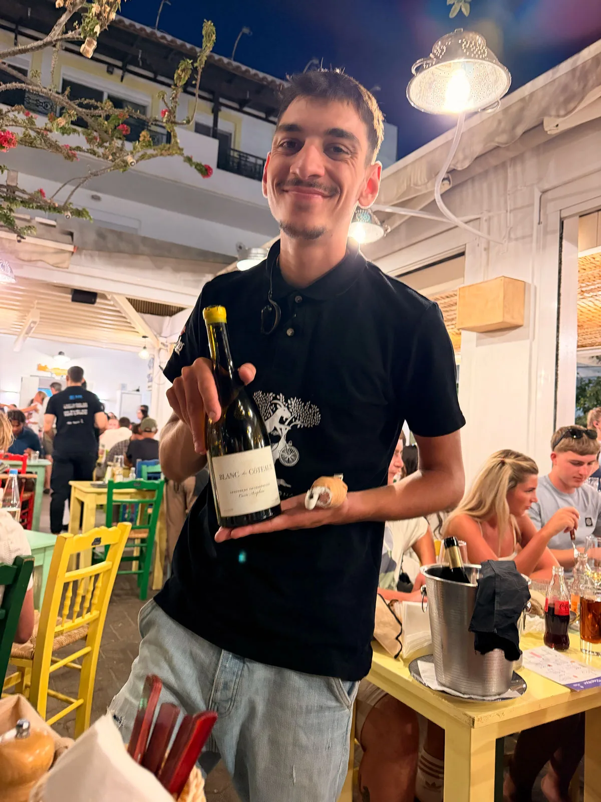 Our smiling waiter at Karnagio Agios Nikolaos holding up the bottle of Blanc des Coteaux
