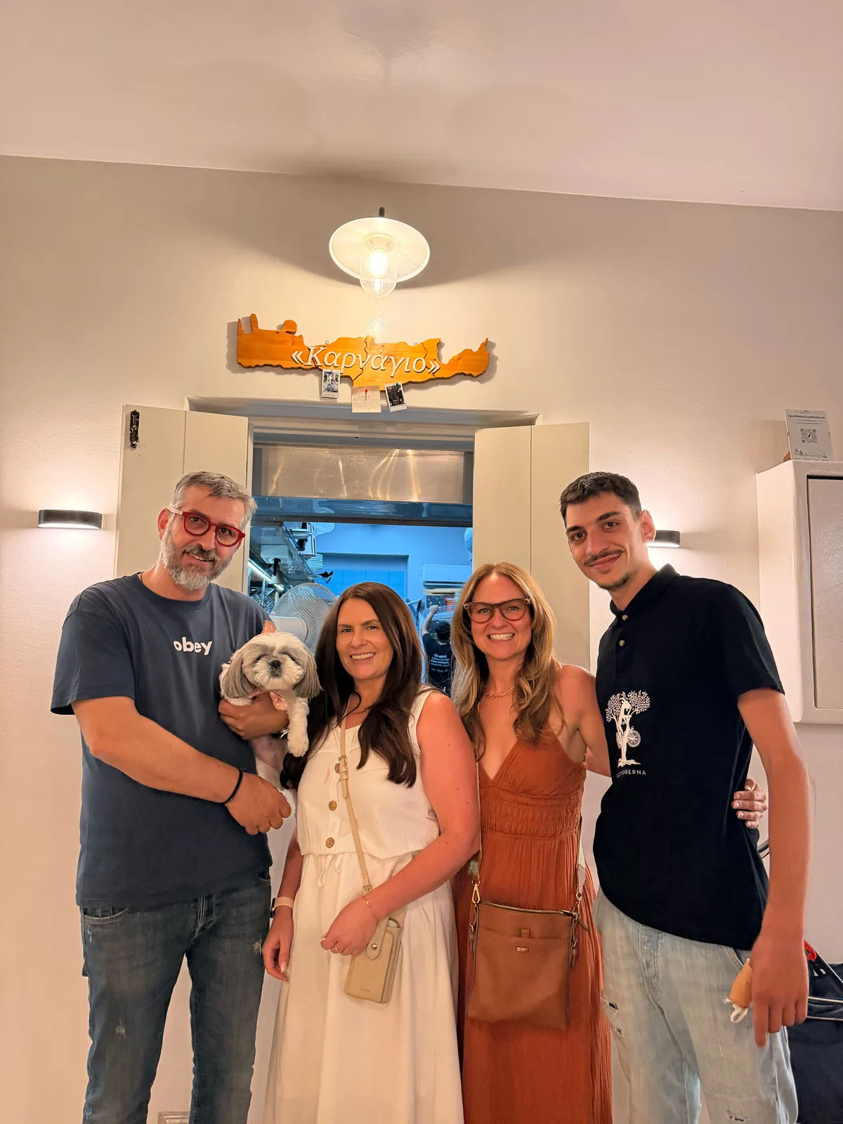 Cheryl and Pam with Daisy the dog and the Karnagio team, lined up under the taverna sign