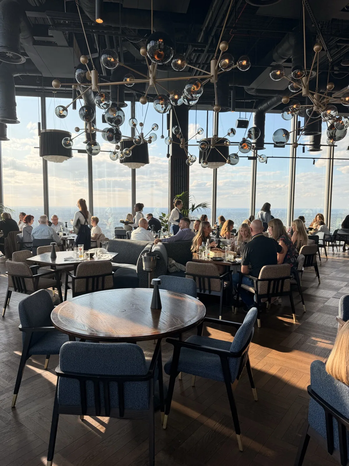 Deep blue velvet chairs and a sculptural cluster of globe pendants beside the floor to ceiling windows at Lucky Cat London