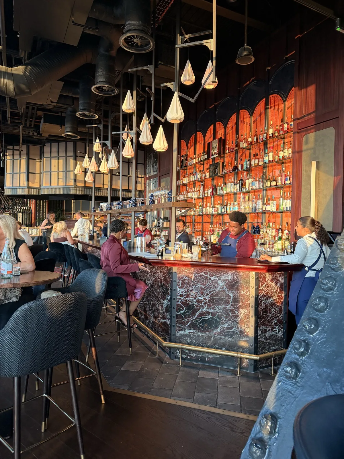 The bar at Lucky Cat 22 Bishopsgate, backlit bottles in red and gold with guests on stools along the counter