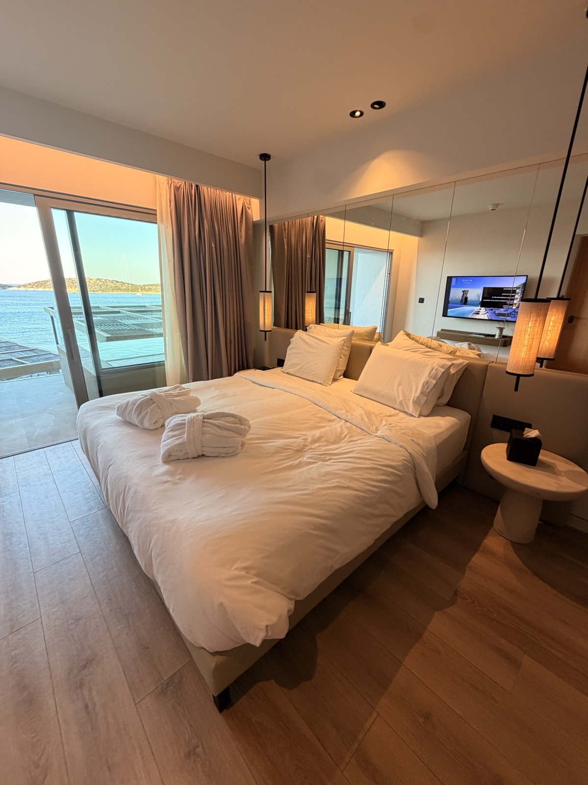 Sea view room at NIKO Seaside Resort Crete with a low wide bed, mirrored wall and the balcony doors open onto Mirabello Bay