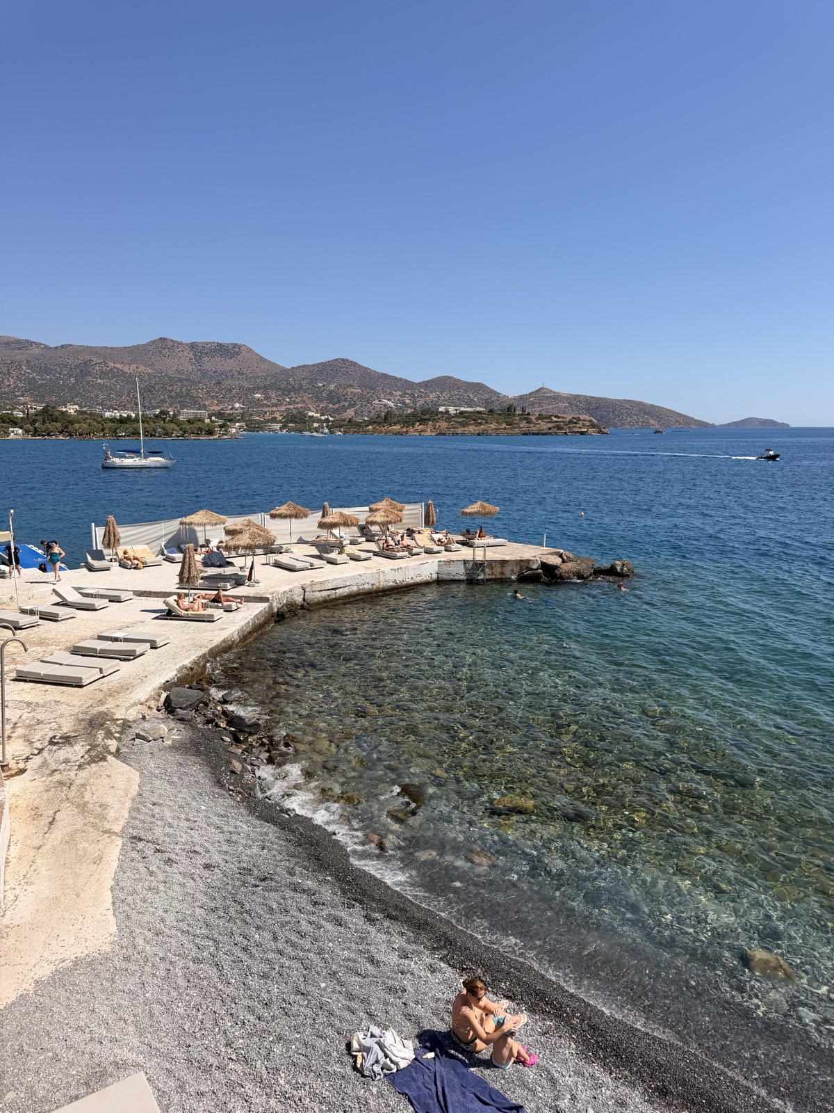 The stony beach and sun loungers on Mirabello Bay below NIKO Seaside Resort in Agios Nikolaos, Crete