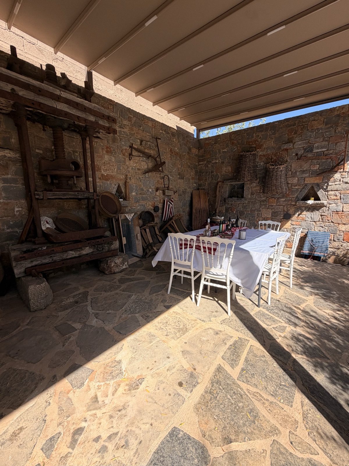 The old wooden olive press under a canopy at Vassilakis Estate, beside a table laid for visitors