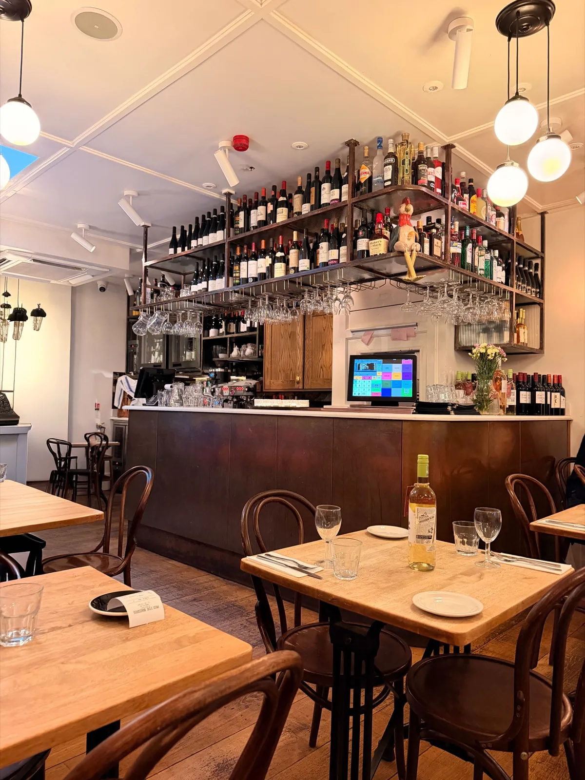 Inside Prix Fixe Brasserie on Dean Street, Soho, laid tables and bentwood chairs beside a vintage Brasserie Lengrand beer poster