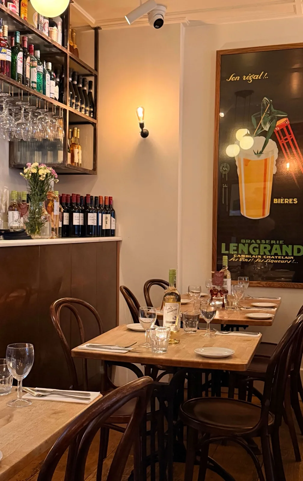 Inside Prix Fixe Brasserie on Dean Street, Soho, laid tables and bentwood chairs beside a vintage Brasserie Lengrand beer poster