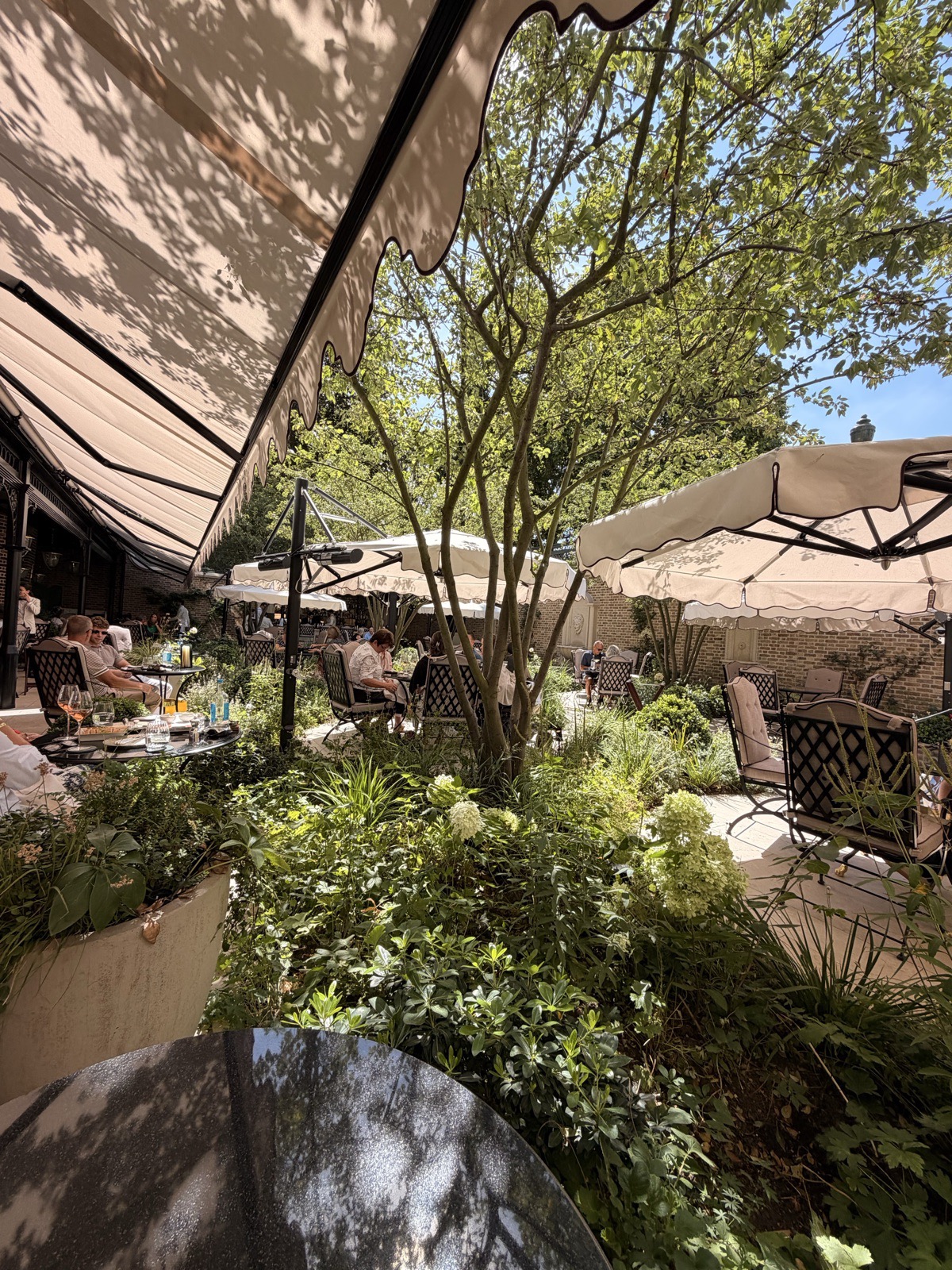 The Secret Garden terrace at The Ritz London on a sunny summer afternoon, shaded by parasols