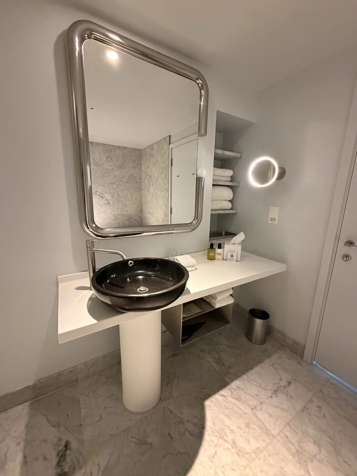 The glossy black basin on its single white pedestal under a huge tubular chrome mirror in the bathroom at Sea Containers London