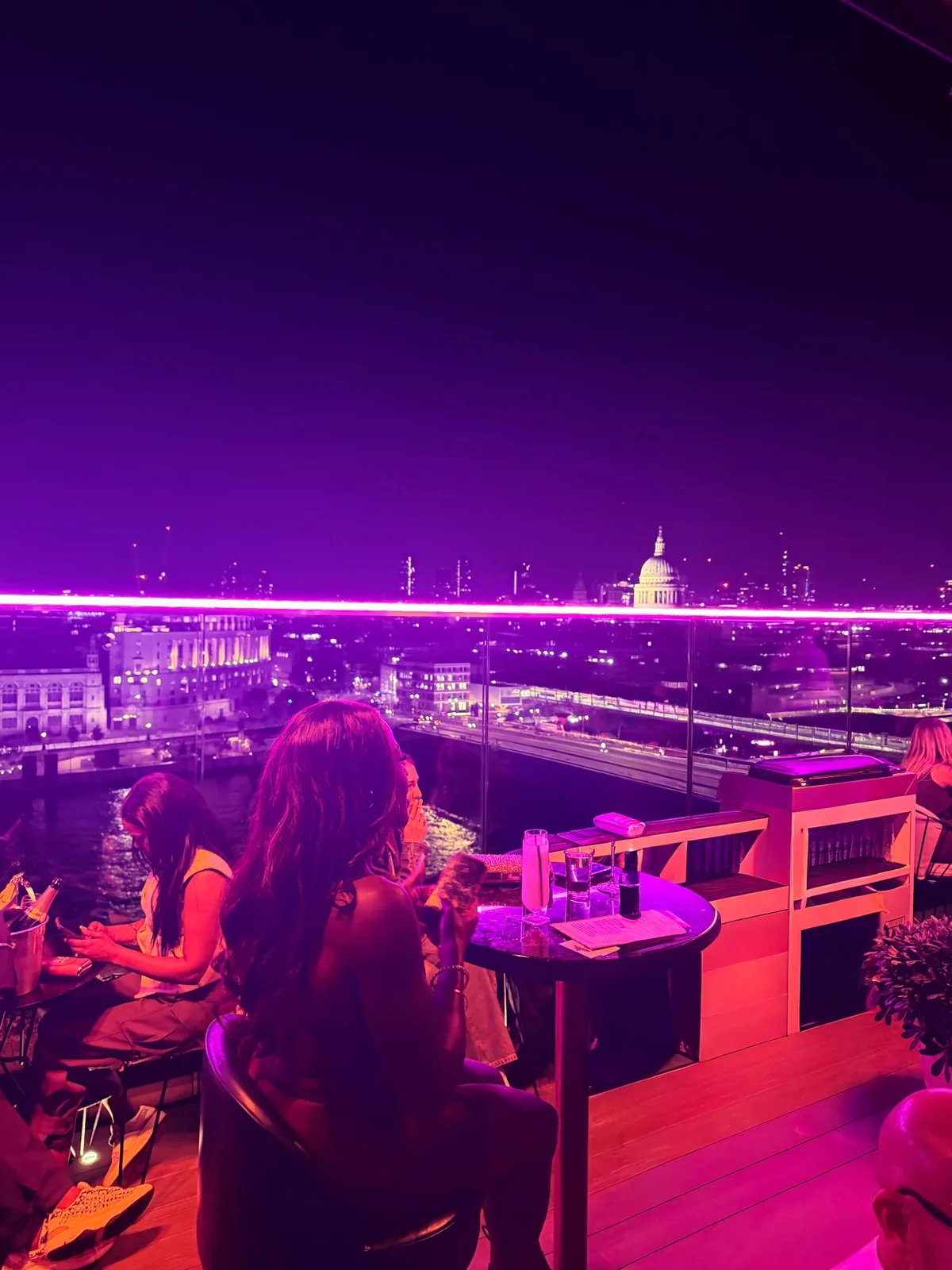 The City of London skyline at night from the 12th Knot rooftop bar at Sea Containers London, the terrace lit with violet neon