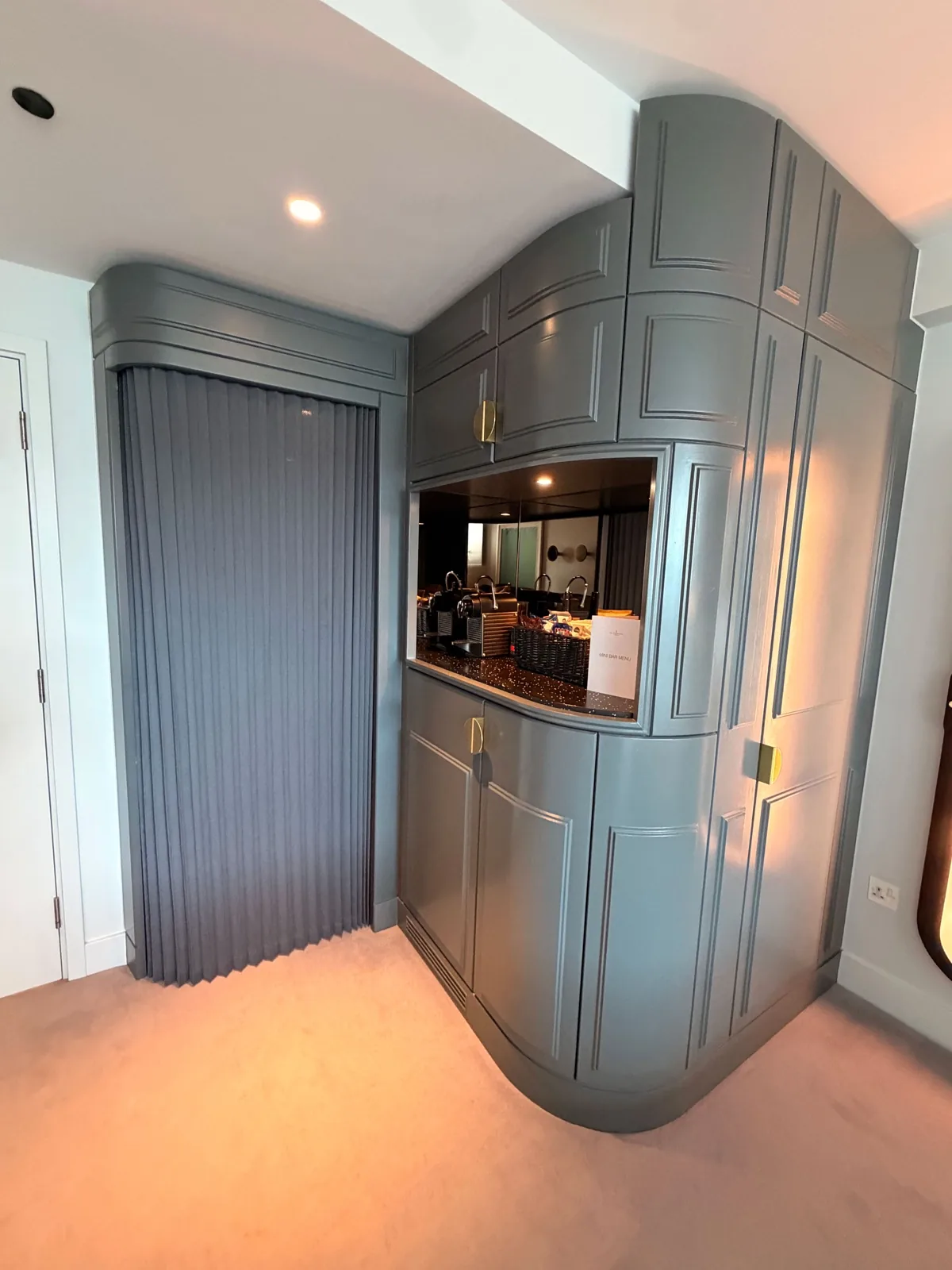 The curved blue grey wardrobe and minibar unit with brass handles in a Sea Containers London room