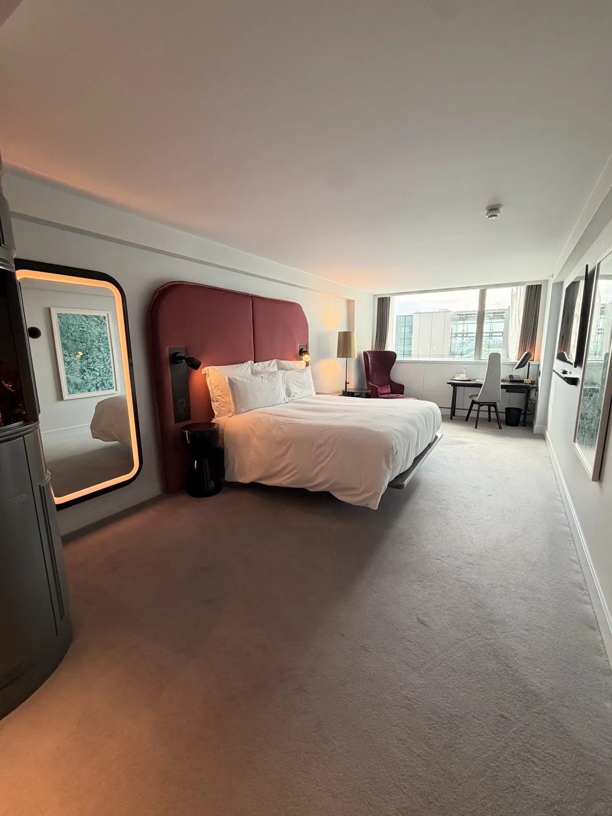 The upgraded room on the 14th floor at Sea Containers London, with a burgundy velvet headboard, a long expanse of carpet and the city through the window