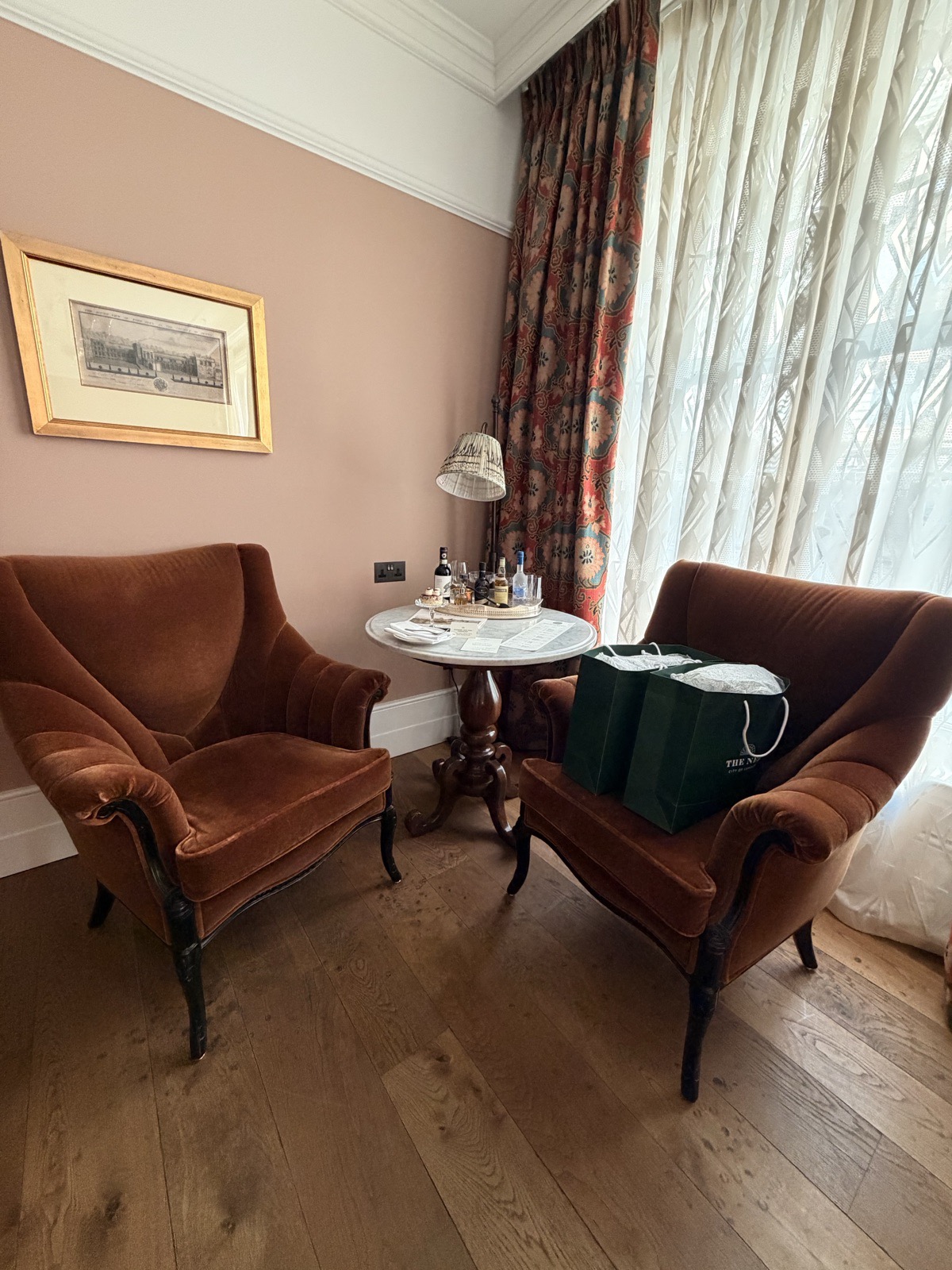 The seating area of a medium room at The Ned, with warm lamps and patterned curtains