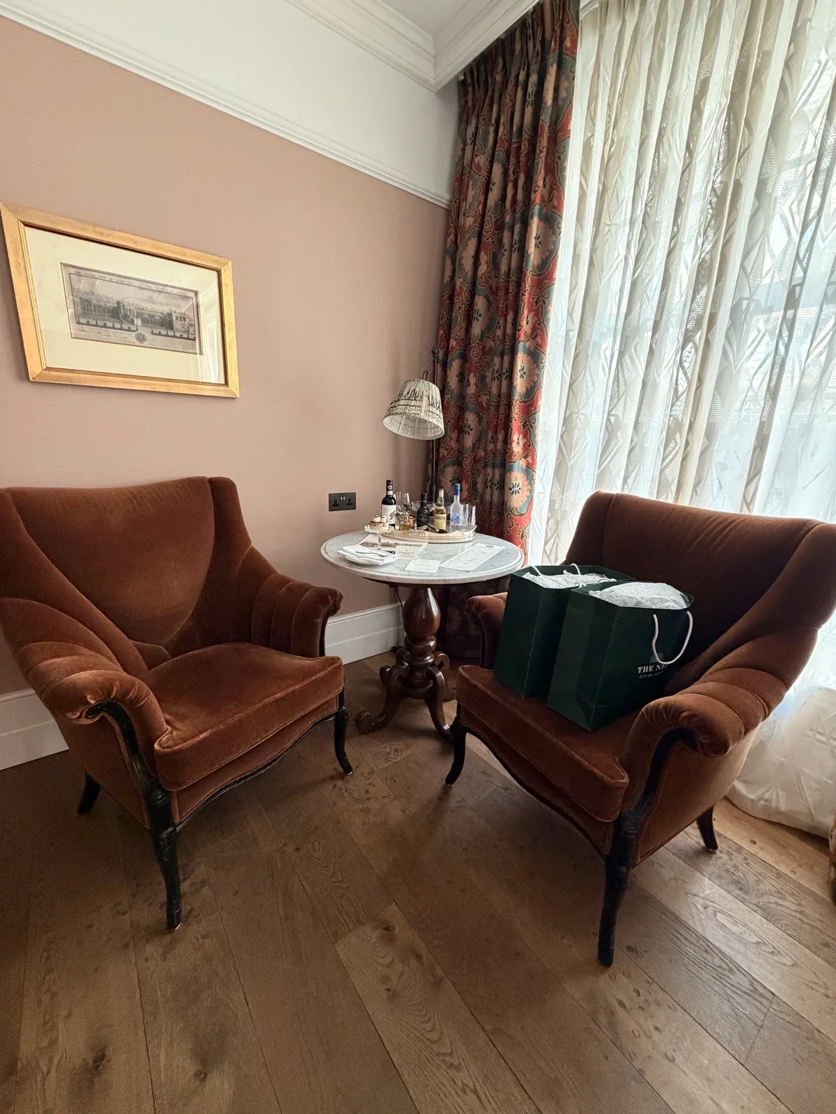 The seating area of a medium room at The Ned, with warm lamps and patterned curtains