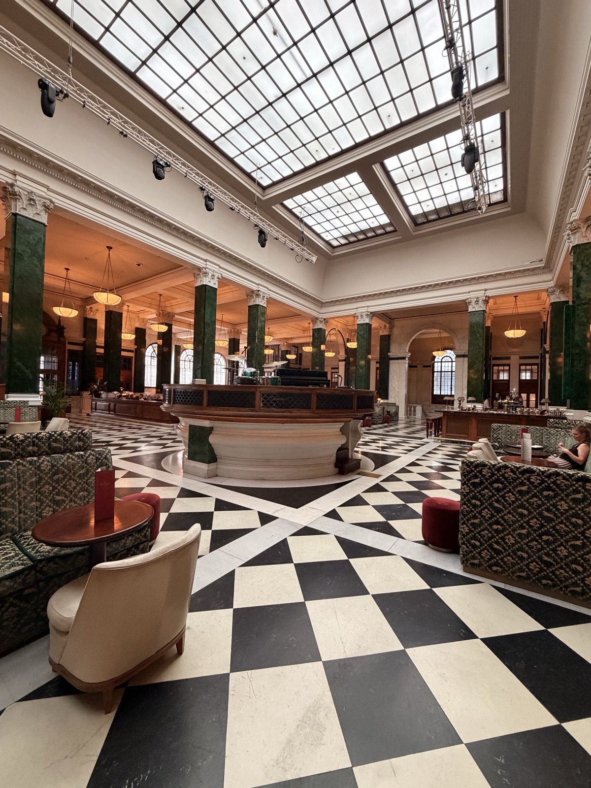 The banking hall at The Ned by day, with its chequerboard marble floor, glazed roof and the Nickel Stage at the centre