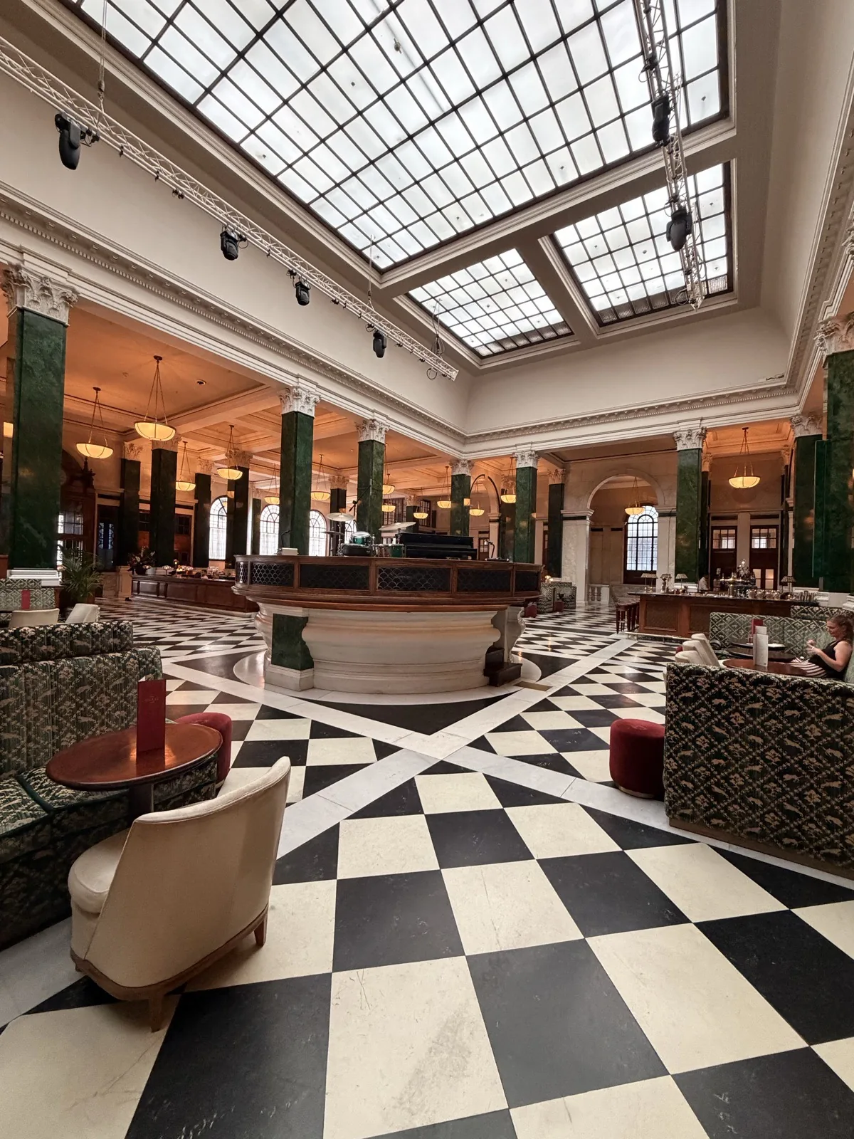 The banking hall at The Ned by day, with its chequerboard marble floor, glazed roof and the Nickel Stage at the centre