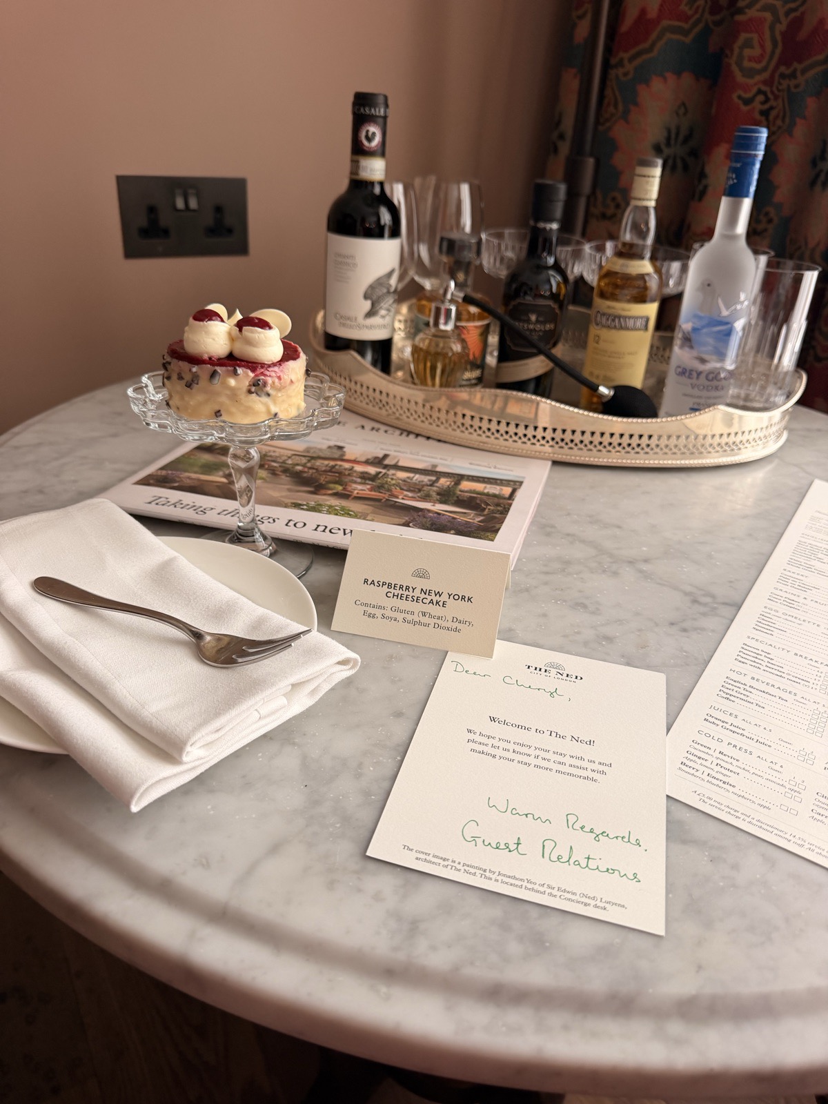 A handwritten welcome note, a raspberry cheesecake and a tray of drinks waiting in the room at The Ned